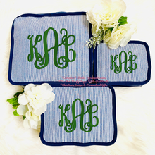 Load image into Gallery viewer, Three personalized monogrammed zippered pouches in a blue and white striped fabric with green embroidered initials, styled with white flowers on a white faux fur background.

